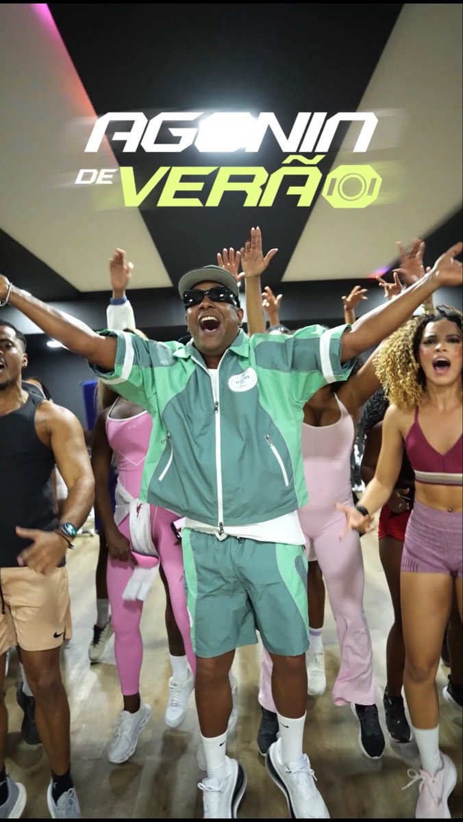 A group of people dancing energetically in a gym setting, with the text 'AGONIA DE VERÃO' displayed in green and white at the top.
