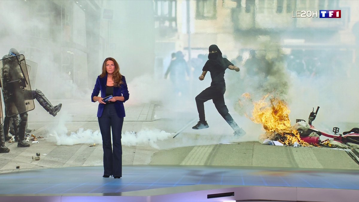 A female news anchor in a blue blazer stands in a TF1 studio with a large screen behind her showing a dramatic protest scene with smoke, fire, a riot police officer with a shield, and a masked figure leaping through the air.
