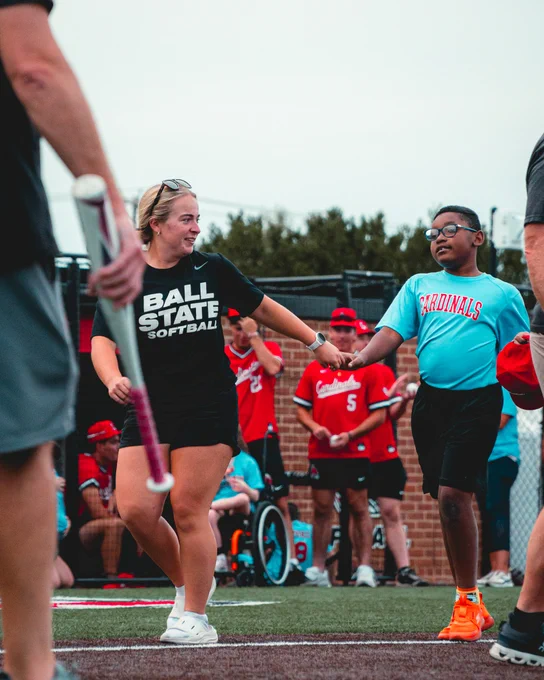 Ball State softball player in a red shirt running with a Miracle League player in a blue shirt