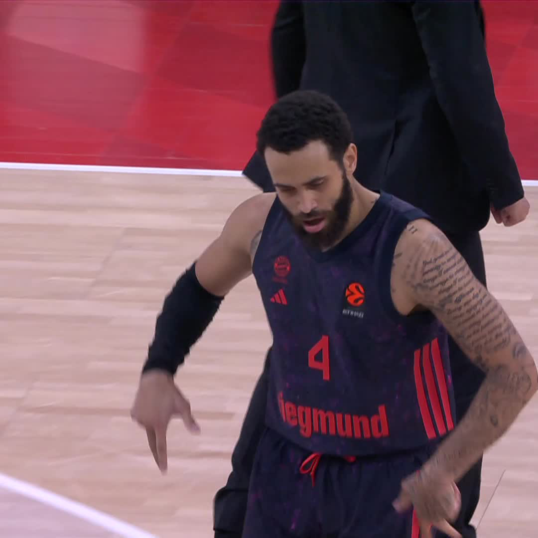 A bearded basketball player wearing a dark jersey with the number 4 and 'Siegmund' branding walks on a court, displaying prominent tattoos on his left arm.
