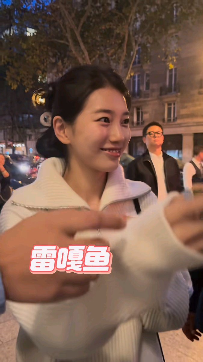 A young woman in a white jacket smiles on a city street at night, with the Chinese text '雷嘎鱼' overlaid on the image.