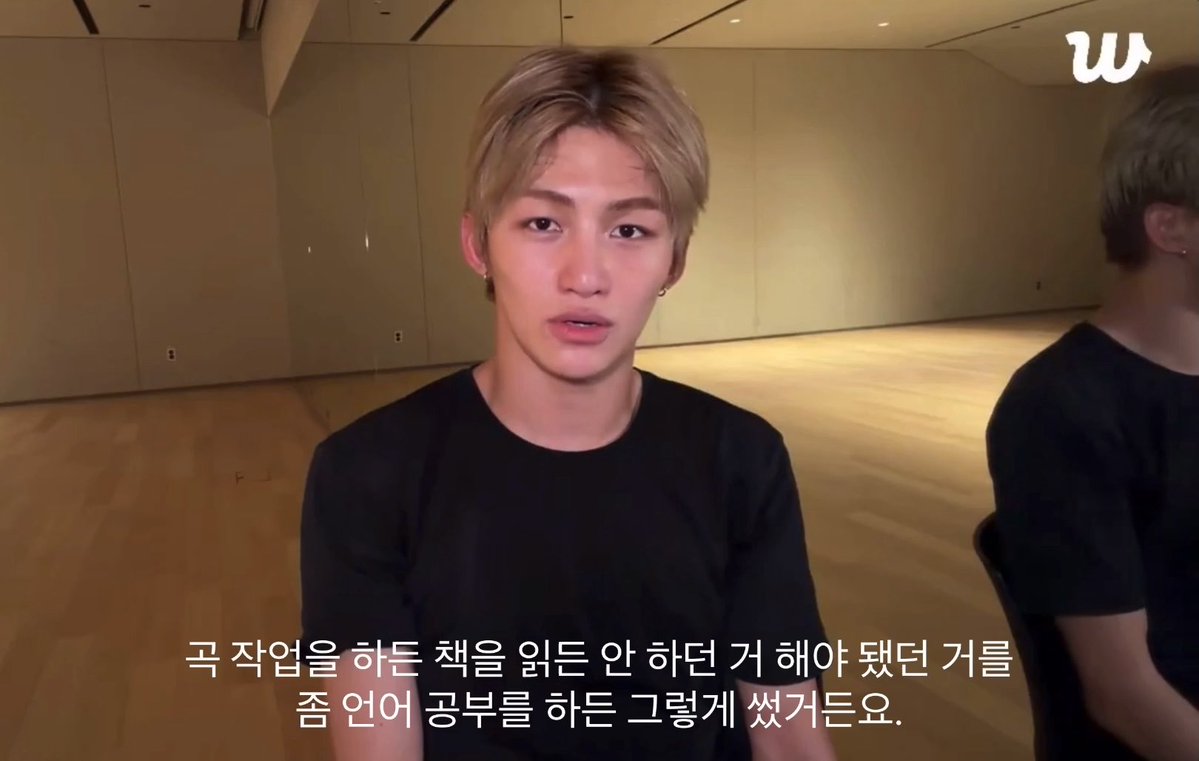 A young man with blonde hair wearing a black t-shirt sits in a dance studio, with Korean subtitles translating roughly to needing to read the book given for this work.
