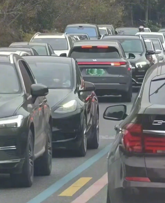 A dense traffic jam on a multi-lane road with numerous black cars lined up bumper to bumper, with one car's brake lights illuminated.