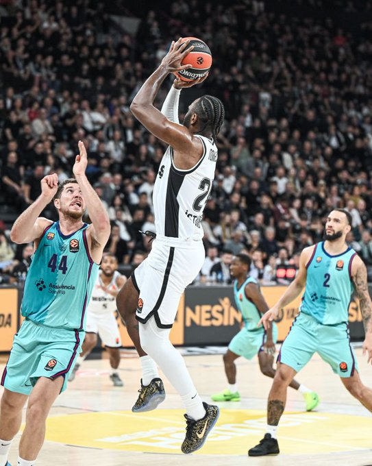 A basketball player wearing a black and white #2 jersey leaps high for a jump shot, with two opposing defenders in teal #44 and #2 jerseys attempting to block him during a EuroLeague game between Beşiktaş and Barcelona. The scoreboard-style post "MS| Beşiktaş: - :Barcelona" indicates this is a matchup between the Turkish club Beşiktaş and the Spanish powerhouse FC Barcelona.