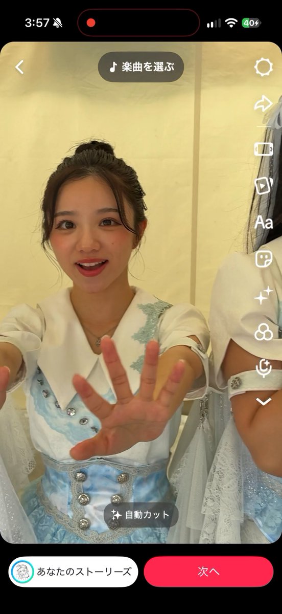 A screenshot of a mobile app interface in Japanese showing a young woman in a blue and white costume reaching toward the camera, with TikTok-like editing options visible.