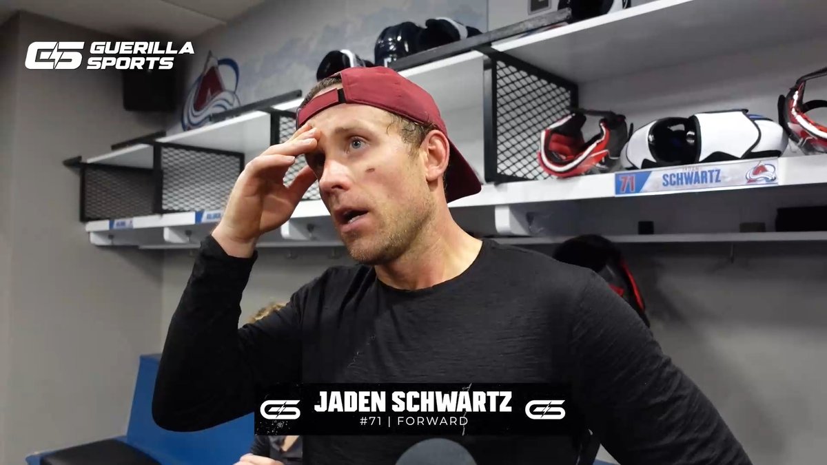 A man wearing a maroon cap backwards stands in a hockey locker room holding his head; on-screen text identifies him as 'JADEN SCHWARTZ #71 | FORWARD' with a 'GUERILLA SPORTS' logo.