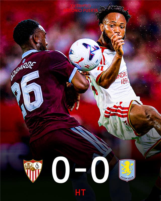 The image shows a close action shot from a football match between Sevilla and Aston Villa, featuring Sevilla's #26 Bogaarde heading the ball against an Aston Villa defender. The graphic displays the halftime score of "0-0 HT" along with both team crests, the Sevilla crest for the #AntonioPuertaTrophy, indicating a goalless first half in the match.