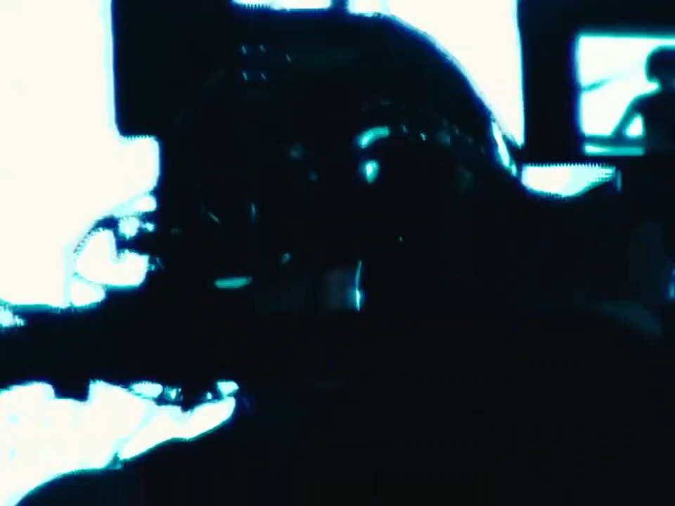 A heavily stylized, dark image with high contrast showing a silhouette of a figure wearing a helmet against a bright teal-tinged background.