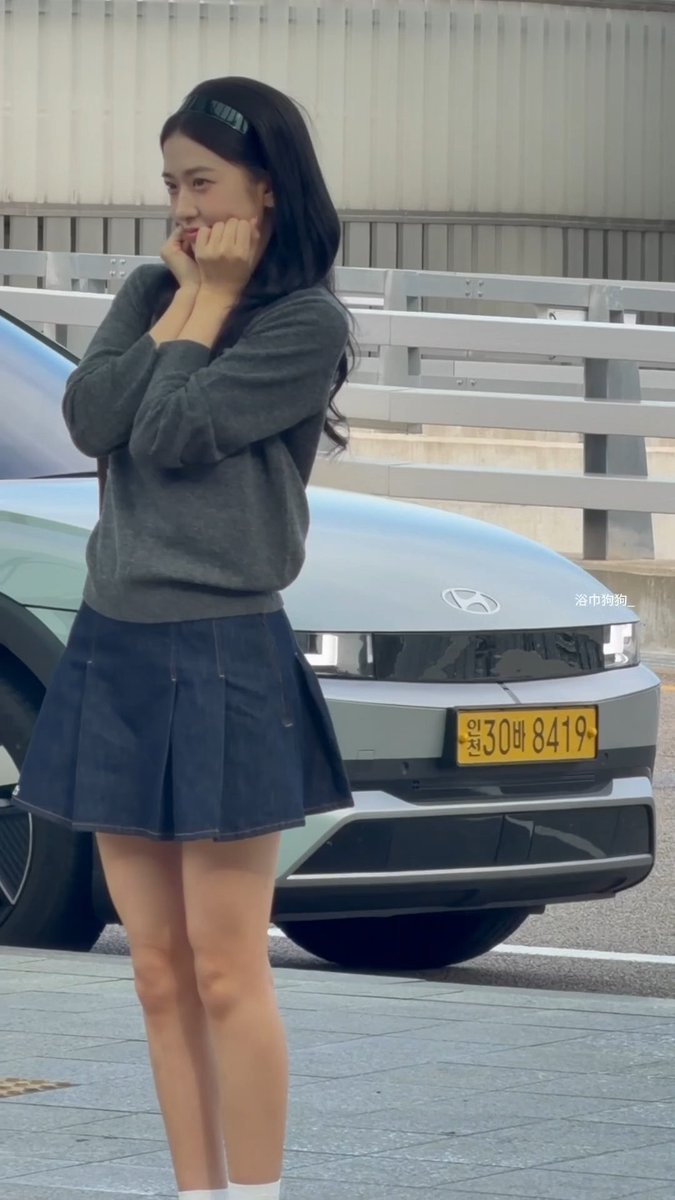 A young woman in a gray sweater and navy pleated skirt standing in front of a light blue Hyundai car with Korean license plate '30바 8419', smiling with her hands near her face.