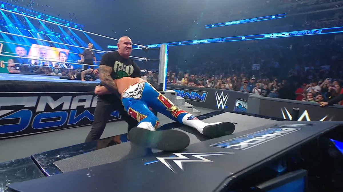 The Undertaker grabs Cody Rhodes at ringside during a SmackDown match, with Randy Orton visible on the entrance ramp screen in the background.