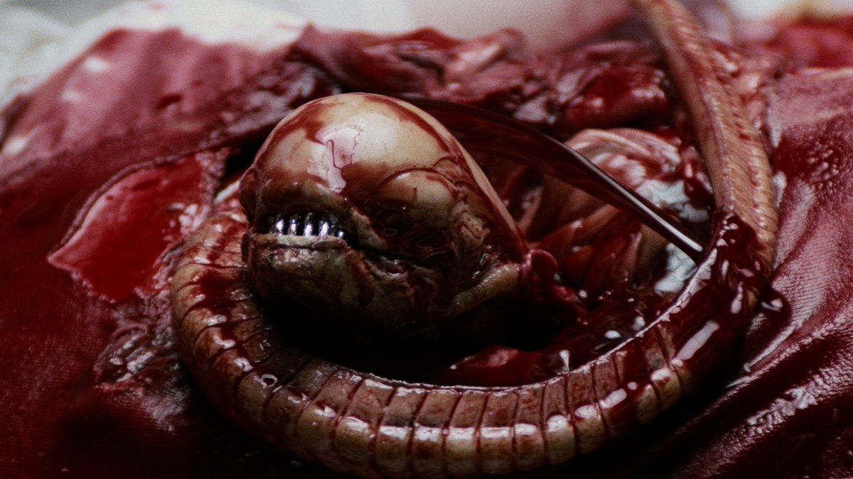 A graphic close-up of the iconic Xenomorph creature bursting from the chest, surrounded by blood and its coiled tail, from Ridley Scott's 1979 sci-fi horror classic *Alien*.