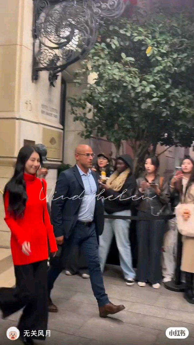 A street scene showing a bald man in a suit walking alongside a woman in a bright red sweater, with fans and onlookers in the background; a watermark reads 'windbell' with Chinese text '无关风月' at the bottom left.