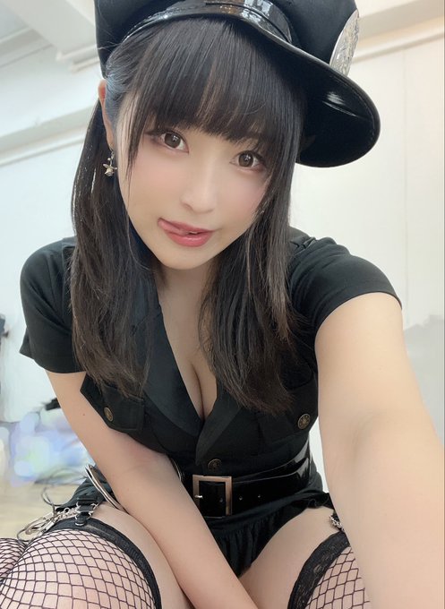 A young woman with dark hair poses for a selfie wearing a black police-style cap and uniform with fishnet stockings.