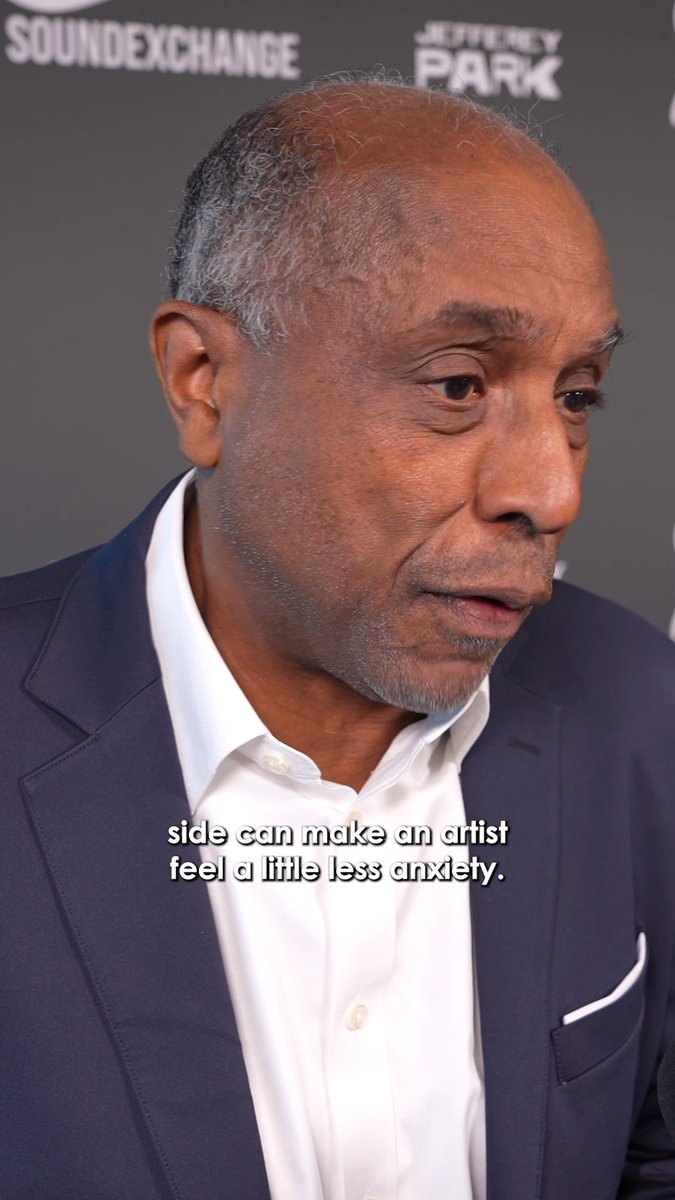 A man in a navy blazer and white shirt speaks at an event, with a backdrop showing 'SOUNDEXCHANGE' and 'JEFFREY PARK' logos, and a caption reading 'side can make an artist feel a little less anxiety.'