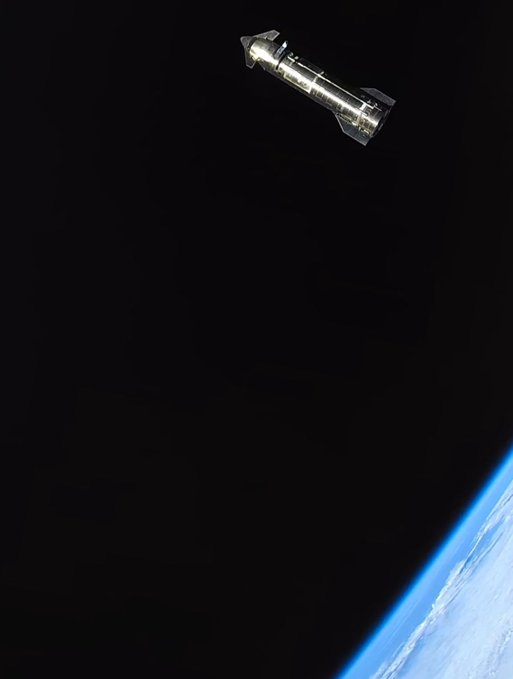 A metallic rocket with fins floats against the black void of space, with the curved blue horizon of Earth visible in the lower right corner, perfectly capturing the surreal sight of Starship drifting high above our planet.