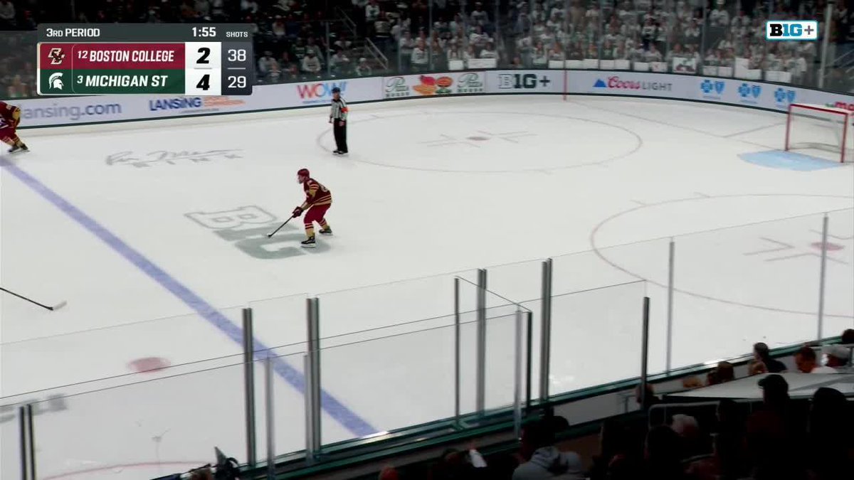 A Boston College hockey player skates toward the empty Michigan State net with 1:55 remaining in the 3rd period, with the scoreboard showing BC trailing 2-4, as the team looks to add to their total. The image captures the moment just before Mason West's empty-net goal extends Michigan State's lead to 5-2.