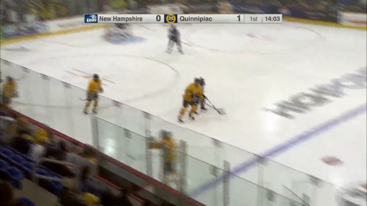 A hockey game broadcast screenshot showing the scoreboard: New Hampshire 0, Quinnipiac 1, in the 1st period with 14:03 remaining, as players in yellow jerseys skate on the ice.