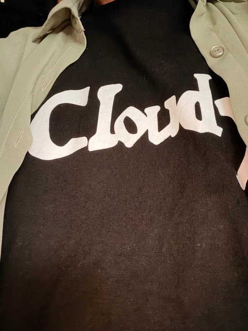 A black t-shirt with the word 'Cloud' printed in white gothic lettering is worn under a light green button-up overshirt.