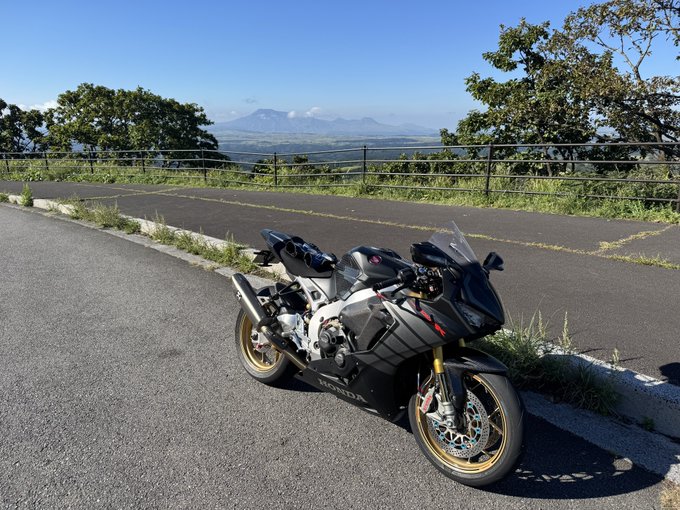 Black Honda sport motorcycle parked on asphalt at a scenic overlook with a view of mountains and a lake in the background.