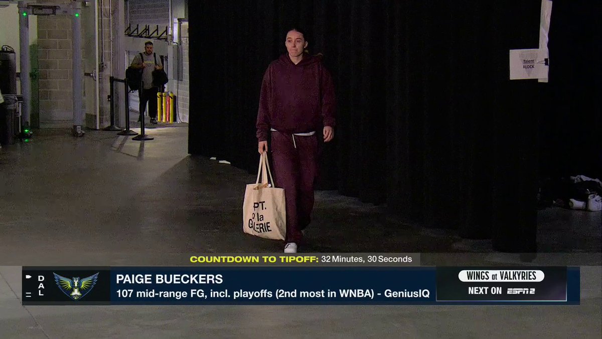 A player in a maroon hoodie walks through a tunnel carrying a "PT. LA GLERIE" tote bag, with an on-screen graphic highlighting Paige Bueckers' "107 mid-range FG, incl. playoffs (2nd most in WNBA)" and a countdown to tipoff at 32 minutes, 30 seconds before Game 3 of Wings vs. Valkyries on ESPN2.