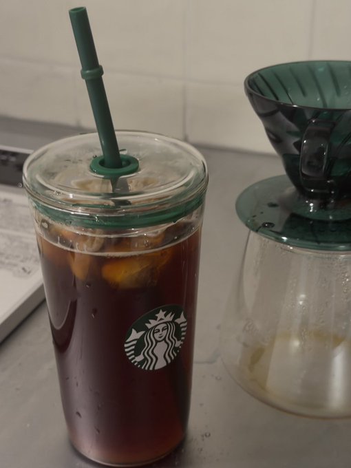 Starbucks iced coffee in a clear cup with green lid and straw next to a green pour-over coffee dripper on a kitchen counter.