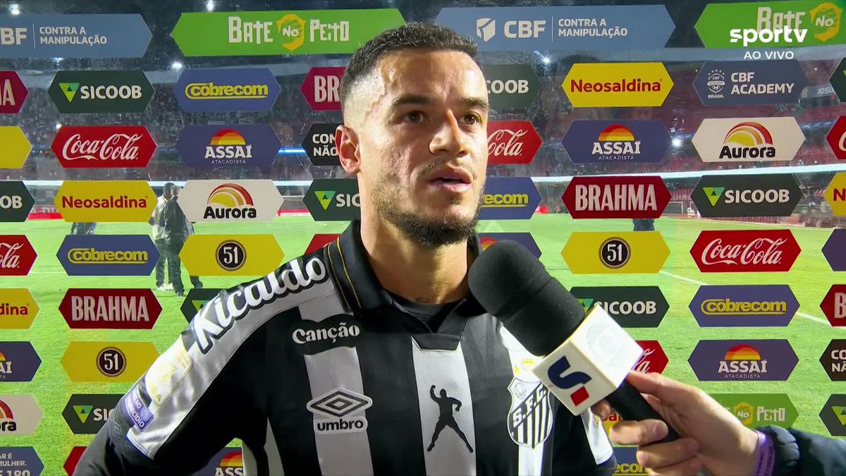 Santos player Coutinho gives a post-match interview on the pitch, speaking into a Sportv microphone in front of a sponsor-laden backdrop featuring Brahma, Coca-Cola, and Sicoob, following his victorious debut for the club.