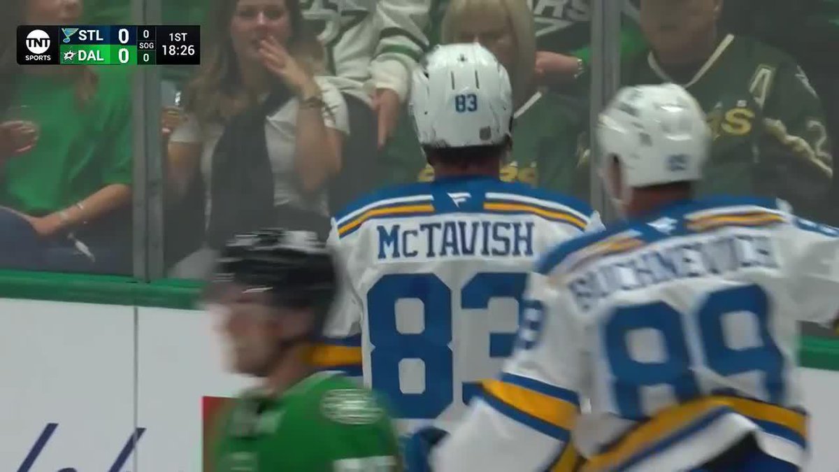 Two St. Louis Blues hockey players, including McTavish wearing #83 and a teammate in #88, stand near the boards while the scoreboard shows STL 0, DAL 0 with 18:26 remaining in the 1st period, likely celebrating McTavish's first goal for the Blues early in the game.