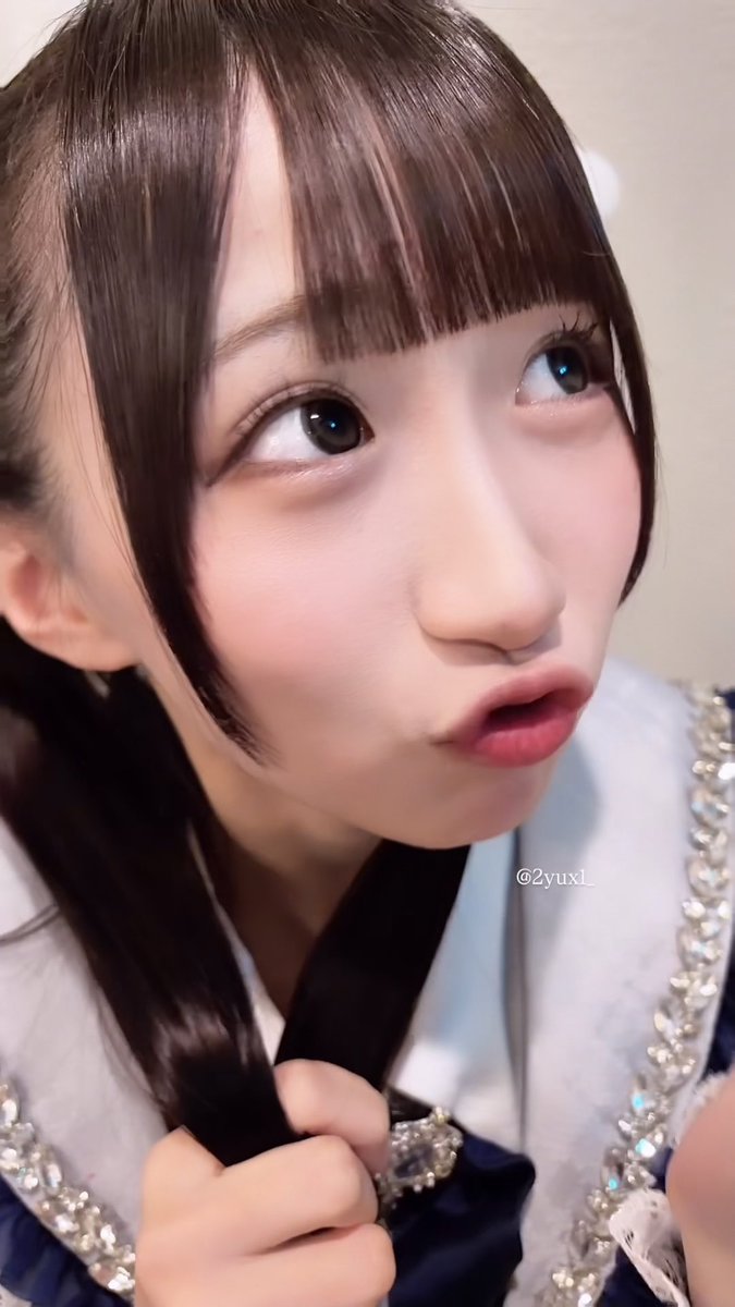 A close-up portrait of a young woman with dark bangs looking sideways with pursed lips, wearing a sparkly white and navy outfit with the watermark '@2yux1_'.