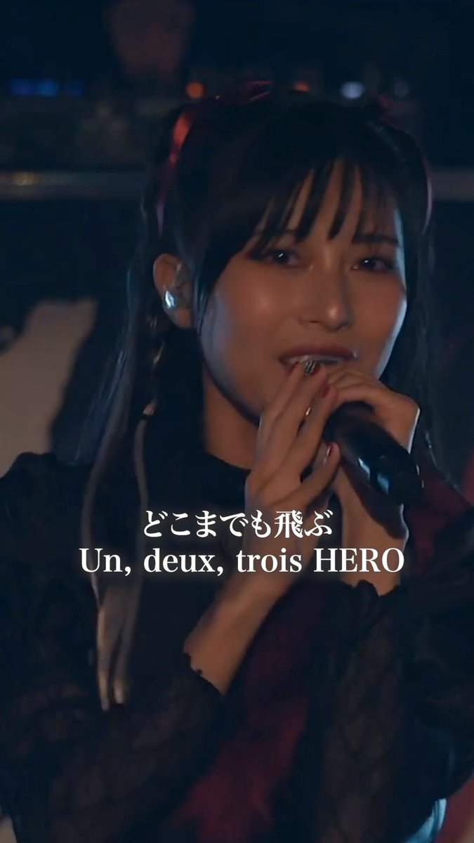 A performer with dark hair and bangs holds a microphone close to her mouth, singing emotionally at what appears to be the Abyssmare 2nd Concert - ALIVE- Osaka Performance. The Japanese text "どこまでも飛ぶ" (Fly as far as I can) and French/English text "Un, deux, trois HERO" are overlaid on the image, referencing hashtags #Abyssmare and #D4DJ.