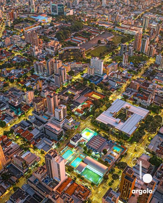 An aerial nighttime cityscape showing illuminated streets, buildings, and a sports complex, watermarked with 'argolo'.
