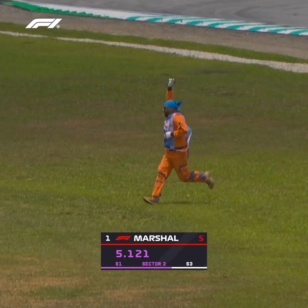 A marshal in an orange suit and blue bandana runs across the grass with one arm raised, as the F1 timing graphic below displays "1 MARSHAL S 5.121 S1 SECTOR 2 S3," humorously reflecting the social media post praising the marshal's quick recovery during the Bahrain Grand Prix.
