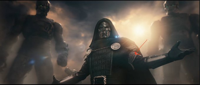 A cinematic image of Doctor Doom from Marvel wearing his signature hooded cloak and metal mask, with his arm extended showing a glowing orange power, flanked by giant statues in a dramatic cloudy setting.