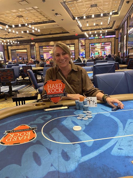 A woman smiling at a blackjack table inside the Hard Rock Casino Cincinnati, with poker chips stacked in front of her.
