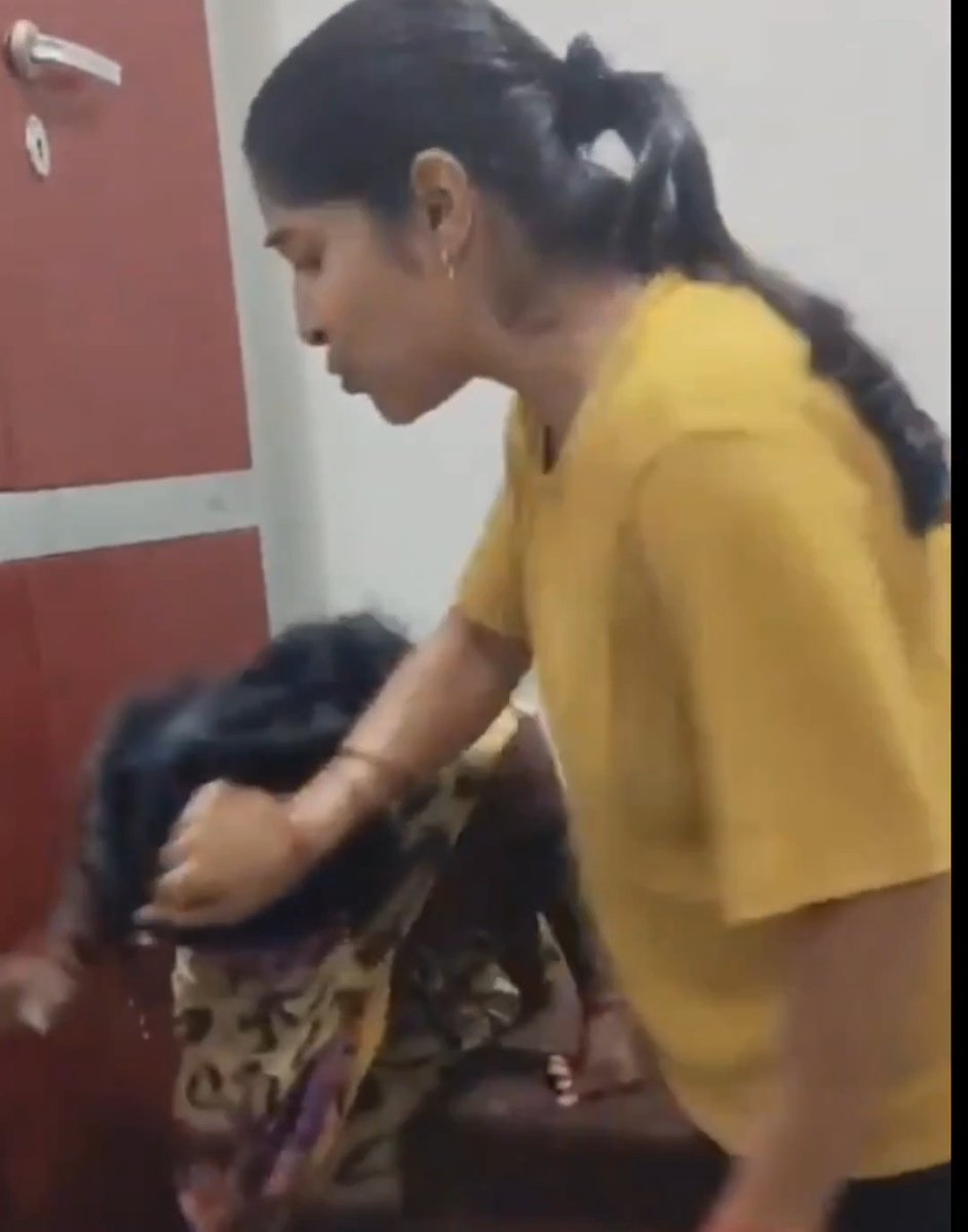 A woman in a yellow shirt strikes another person, who is bent over in apparent distress, inside a room with red doors. The image visually depicts the alleged attack on a Dalit domestic worker described in the accompanying post, showing the physical violence referenced in the claims of barbarity and caste-based aggression.