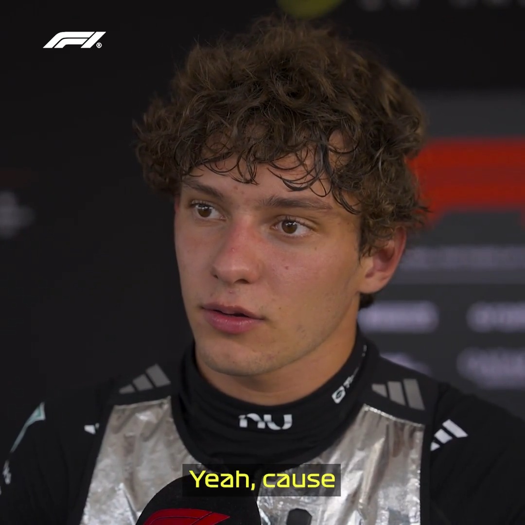 A young Mercedes-AMG F1 driver with curly brown hair, wearing a black and silver racing suit, looks surprised during a post-qualifying interview at the Bahrain GP, with the subtitle "Yeah, cause" visible as he reacts to learning he'll start P3 on Sunday.