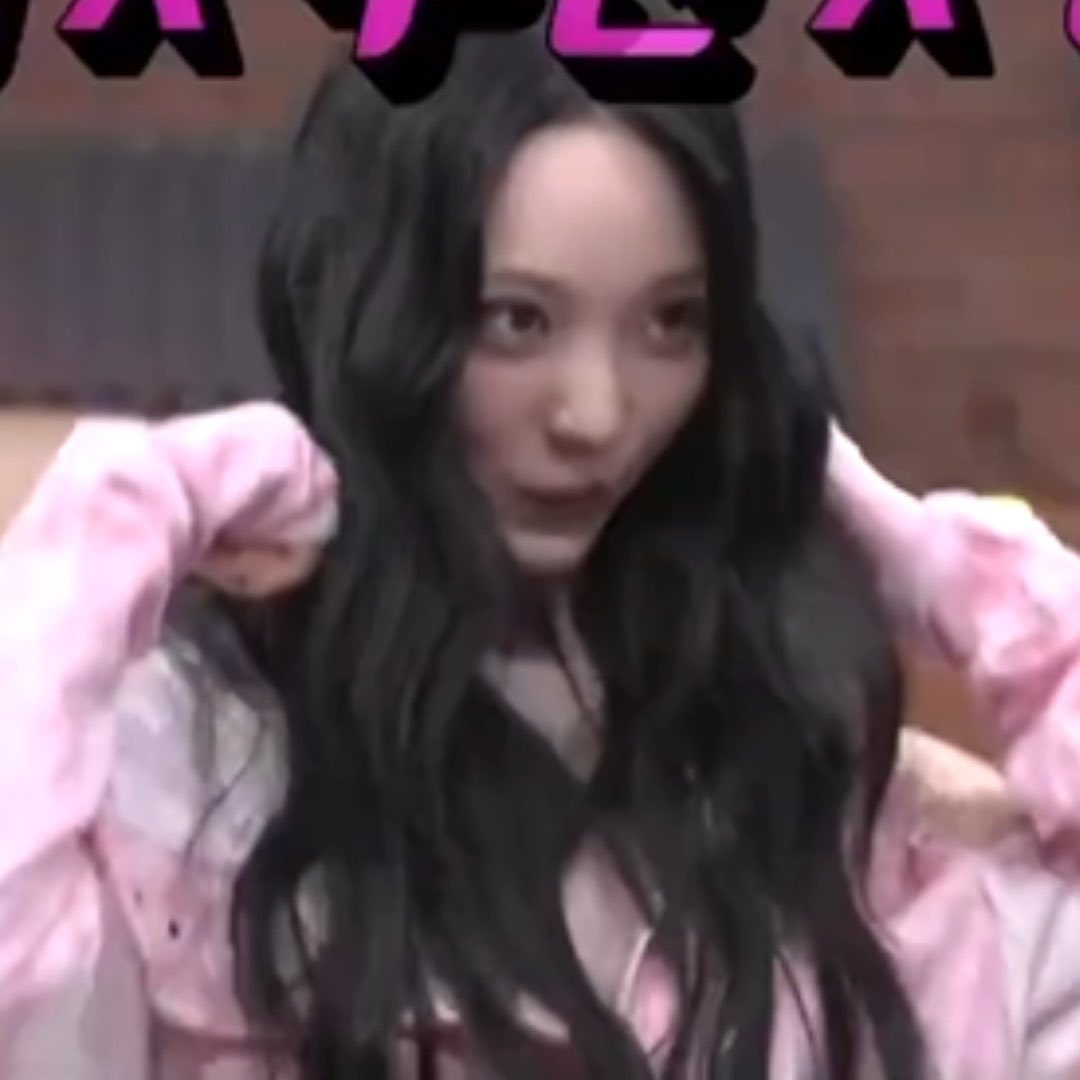 A young woman with long dark hair wearing a pink jacket looks at the camera in what appears to be a video call or livestream screenshot.