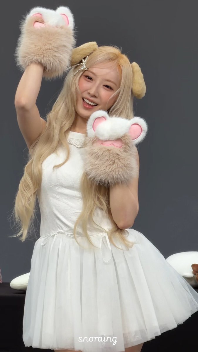 A young woman with long blonde hair wearing a white dress, smiling and posing with fluffy paw-shaped gloves and animal ear headbands, with the watermark 'snoraing' at the bottom.