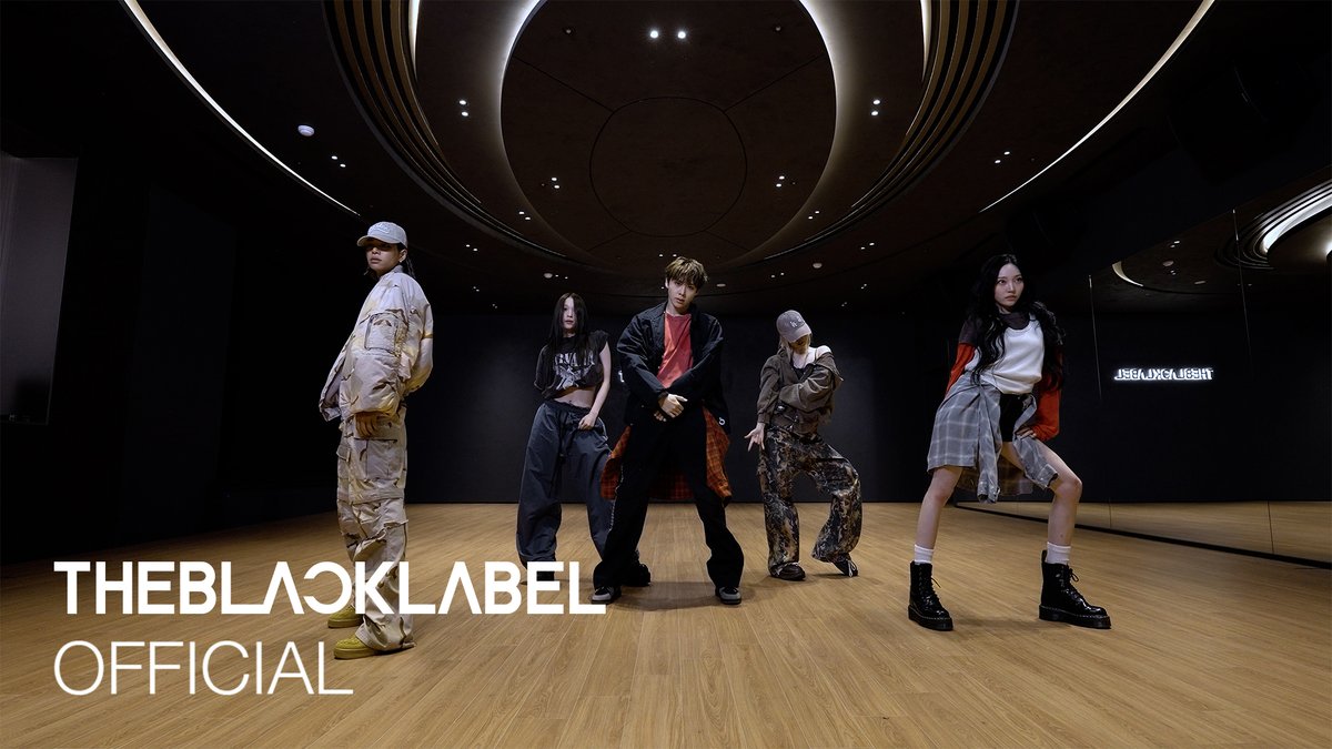 A promotional photo for 'THEBLACKLABEL OFFICIAL' showing five K-pop artists in streetwear poses inside a sleek, modern room with curved ceiling lighting and wooden flooring.