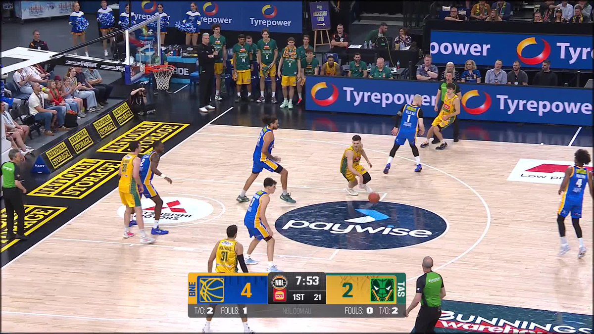 A National Storage branded basketball court features a game between the Brisbane Bullets (BRL) and Tasmania JackJumpers (TAS) with a scoreboard showing BRL leading 4-2 at 7:53 in the 1st quarter, as a Tasmania player in yellow drives toward the basket while guarded by Brisbane players in blue.