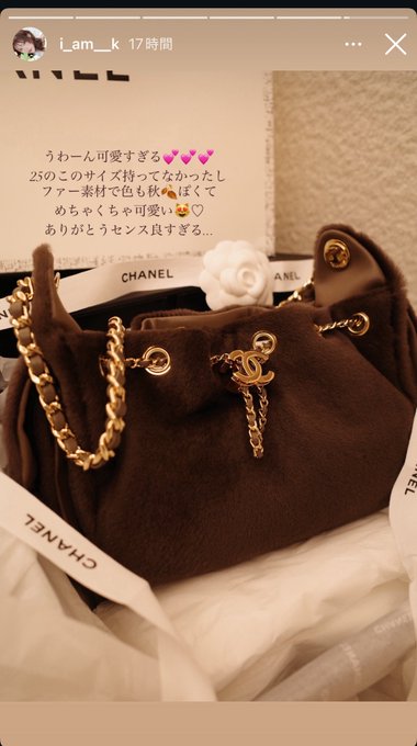 A Chanel 25 handbag in brown suede with gold chain detailing and a signature CC charm is displayed alongside its branded dust bag and a white camellia flower, with Japanese text praising the gift giver's refined taste. The Instagram story from user "i_am_k" highlights the luxury item's material quality and elegant design, connecting to the post's admiration for Kihho-chan receiving high-end gifts from someone with impeccable taste.