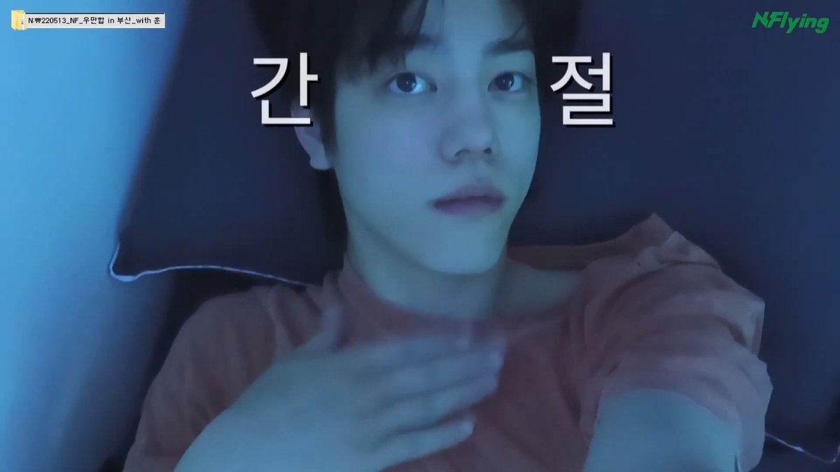 A close-up of a young man lying down in blue-toned lighting wears an orange shirt, with Korean text '간 절' overlaid and 'NFlying' logo in the corner, plus a tag reading 'N₩220513_NF_우선협_in 부산_with 조'.