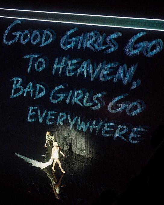 A stage backdrop displays the large blue text "GOOD GIRLS GO TO HEAVEN BAD GIRLS GO EVERYWHERE," while two performers are visible on the dark stage below.