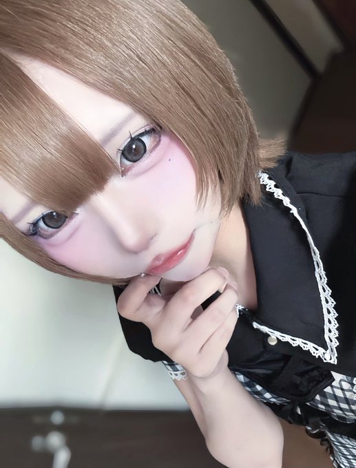 A close-up selfie of a person with a short brown bob hairstyle wearing a black dress with white lace trim, resting their hand near their face.