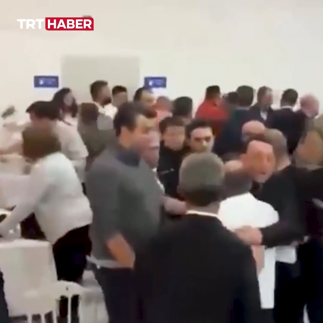 A blurry news clip from TRT HABER showing a chaotic scene with a crowd of people, including men in suits and uniforms, in what appears to be an indoor public setting.