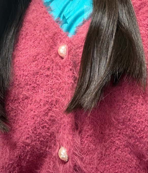 A close-up of a pink fuzzy sweater with pearl-style buttons, partially covered by dark hair against a teal background.