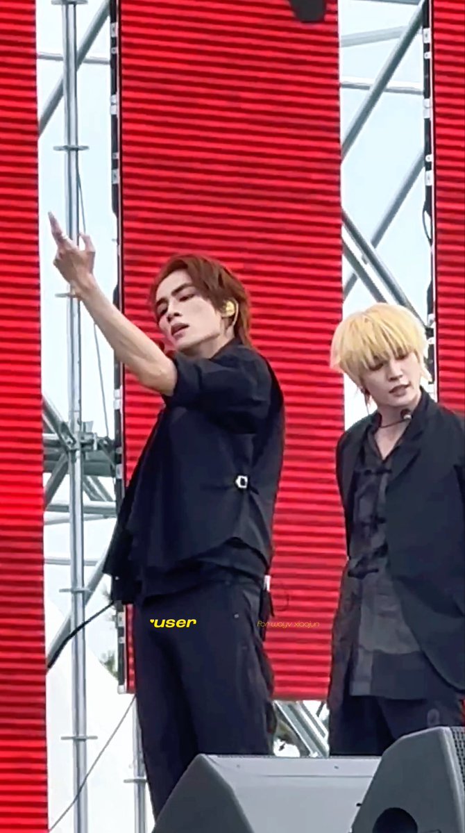 Two male performers on stage in black outfits, one with brown hair gesturing with his arm raised and the other with blonde hair, set against a red LED background; watermarked 'user' and 'fy.wujun.xiaojun'.