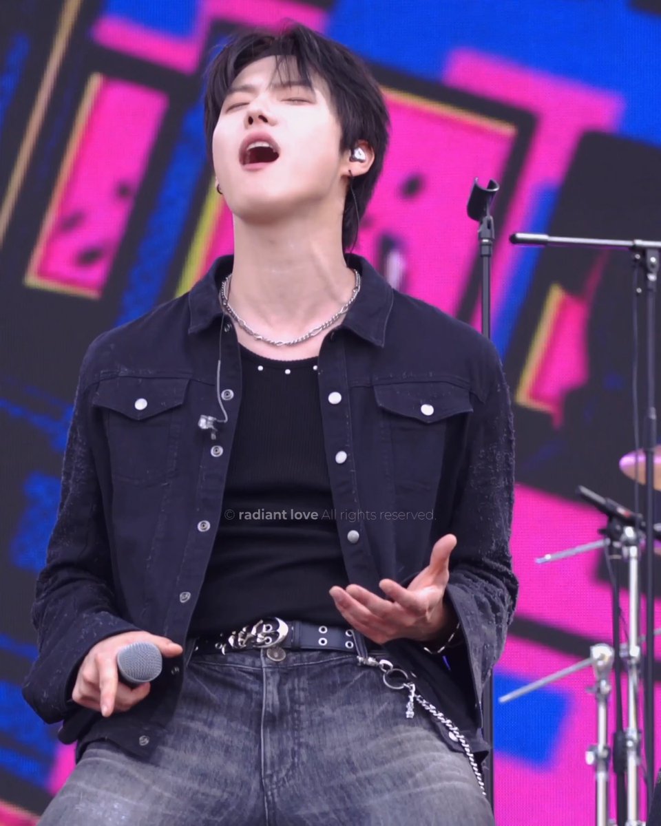 A male performer sings passionately on stage with his eyes closed, wearing a black denim jacket and an in-ear monitor, with a watermark reading '© radiant love All rights reserved.'