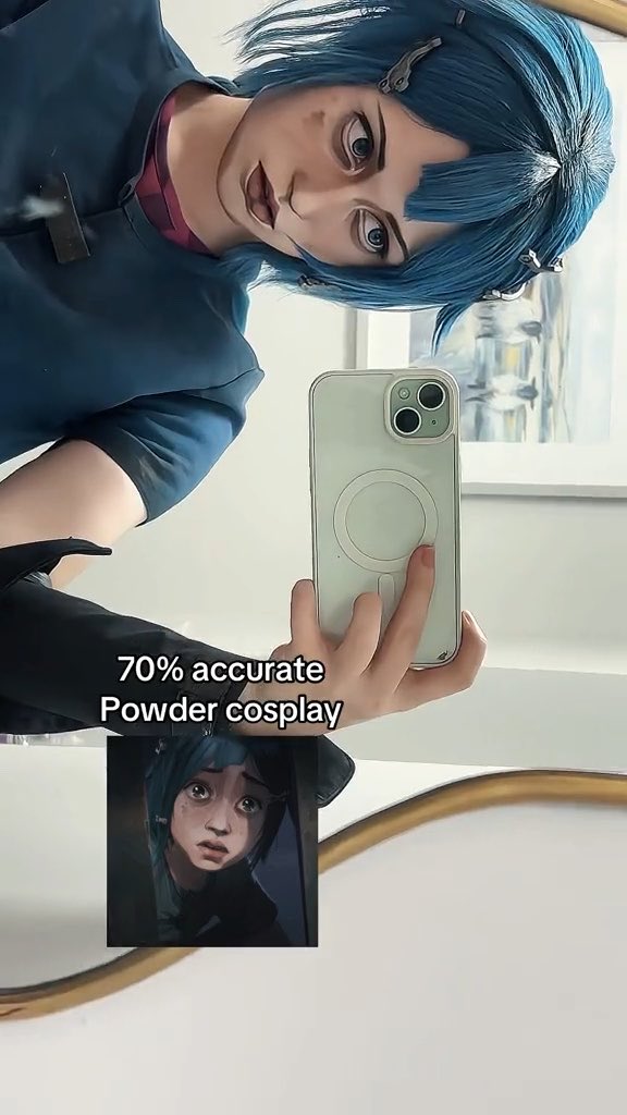 A cosplay photo featuring a person with blue hair holding a phone to take a mirror selfie, with text overlay reading '70% accurate Powder cosplay' and a small inset reference image of the Powder character from Arcane.