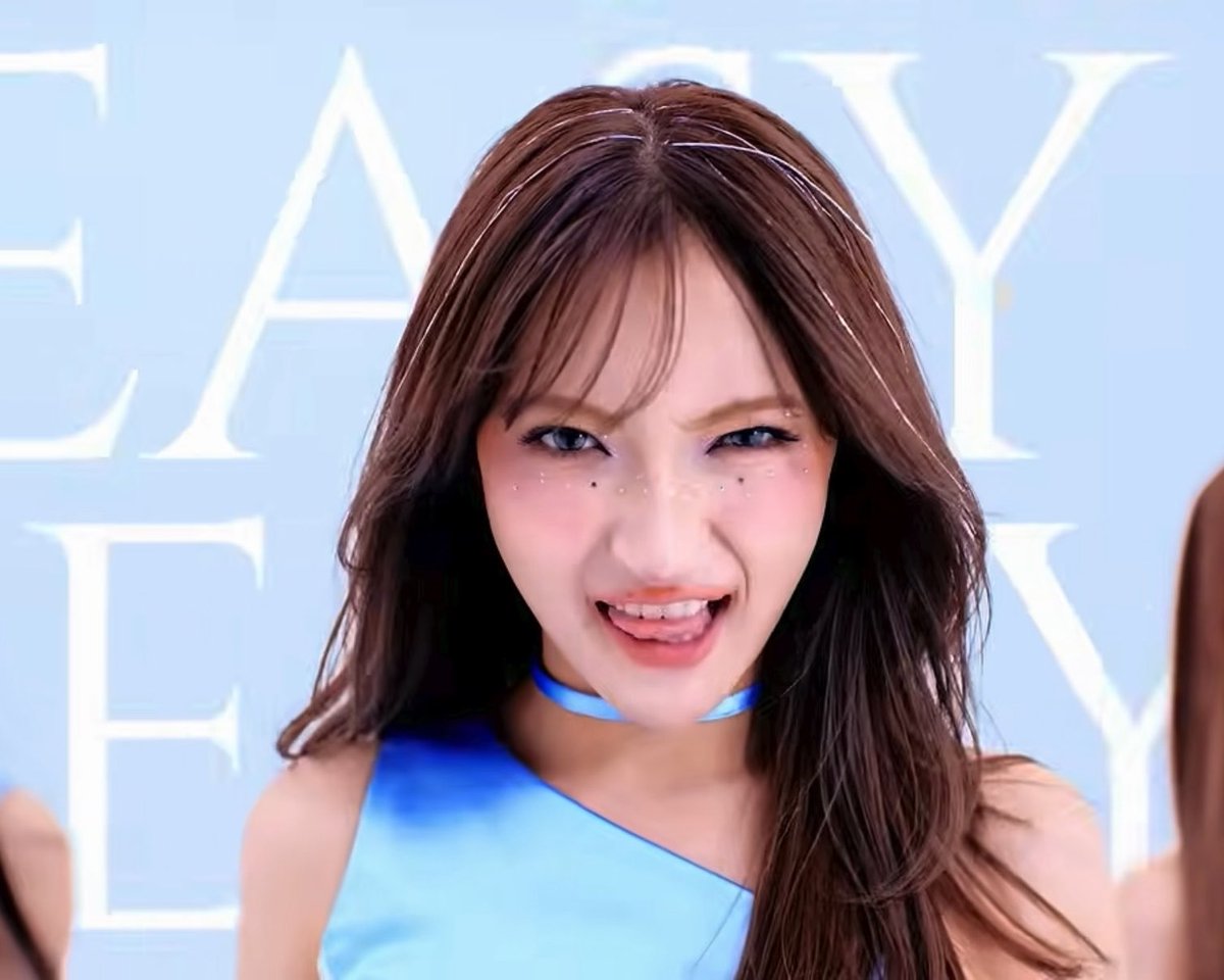 A young woman with brown hair and decorative face gems smiles playfully at the camera, wearing a blue top and matching choker against a light blue background with white text.