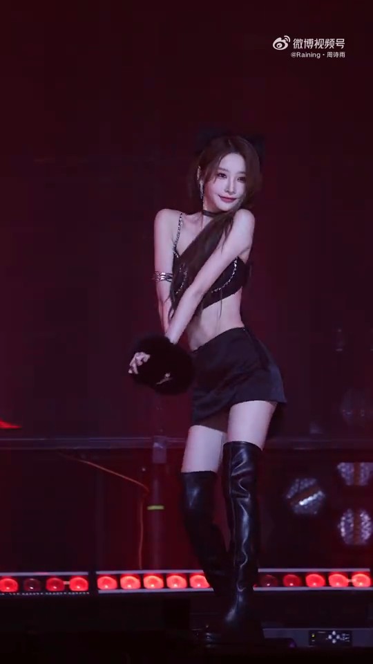 A female performer with long dark hair performs on stage in a black crop top, skirt, and thigh-high boots, with a Weibo watermark visible in the upper right corner.